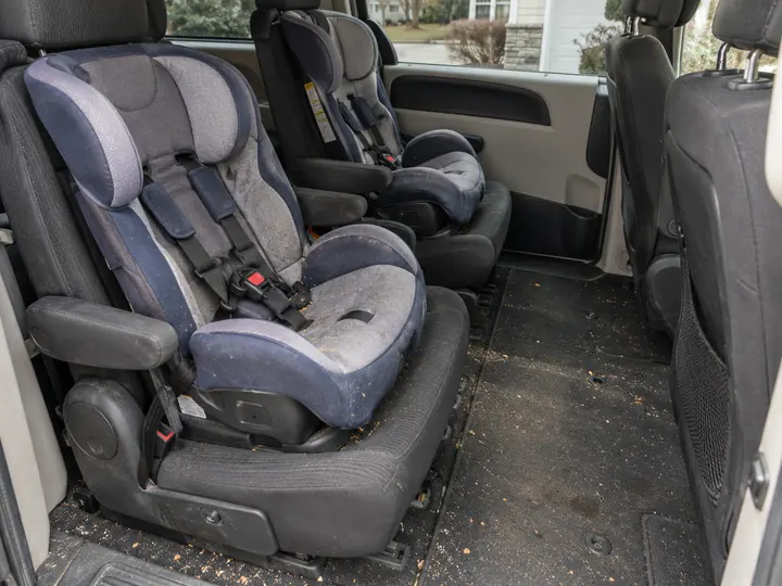 Back row of a family minivan with a child's car seat, crumbs and dirt across the floor, before the Reset